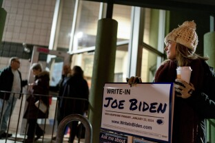 Ashley Marcoux stands outside a polling site with a campaign sign supporting President Joe Biden as a write-in candidate.